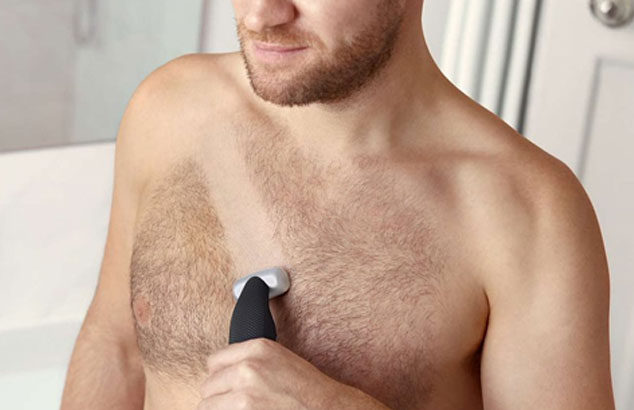 Close-up of a man&rsquo;s hairy chest with stripe being shaven across by an electric shaver he is holding.